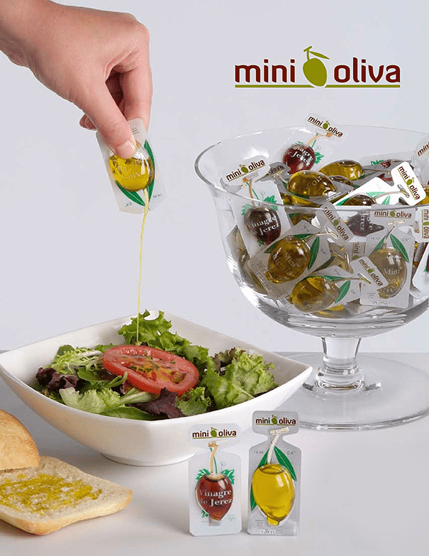 Een mini-olijvenverpakking op een salade, samen met een glazen pot vol mini-olijven.