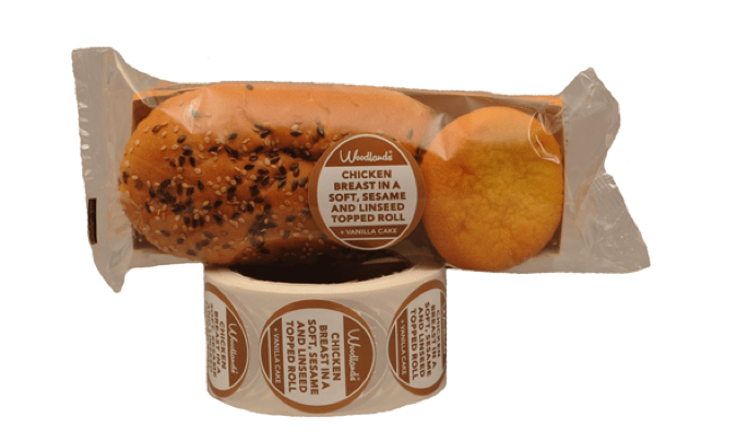 Een pakket met bereide sandwiches met een etiket, staand op een rol van hetzelfde etiket.