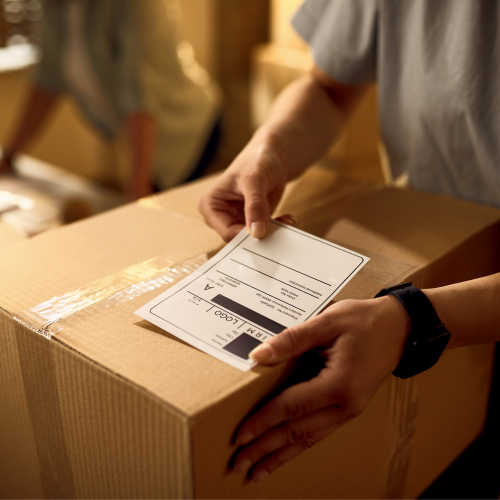 Hände, die ein Etikett auf ein Paket aufbringen.