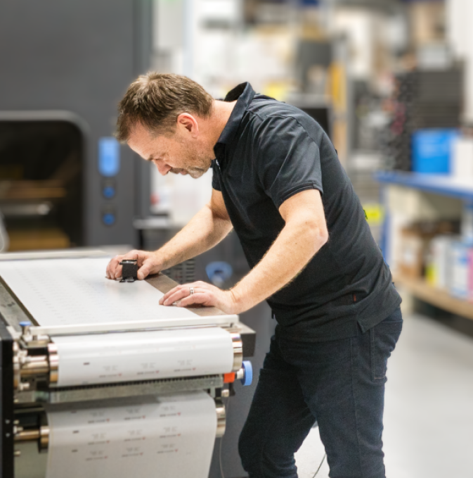 Man operating a label printing machine in a production setting.